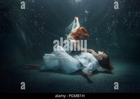 Junge Frau auf der Unterseite unter Wasser liegt, eine andere Frau hält ihre Hand am Hals. Stockfoto