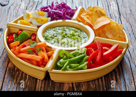 Grüne Salsa verde und mexikanischen Satz von gehackten frischen Gemüse, hartgekochte Eier und Pommes in Schalen auf alten rustikalen Holzbrett. Zutaten für Tacos, Stockfoto