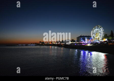 Nachtunterhaltung und Entspannung am Strand des Schwarzen Meeres mit Attraktionen, weißem Riesenrad, Trampolin in einer hellen, blauen, gelben Farbe. Stockfoto