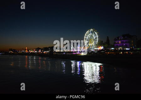 Nachtunterhaltung und Entspannung am Strand des Schwarzen Meeres mit Attraktionen, weißem Riesenrad, Trampolin in einer hellen, blauen, gelben Farbe. Stockfoto