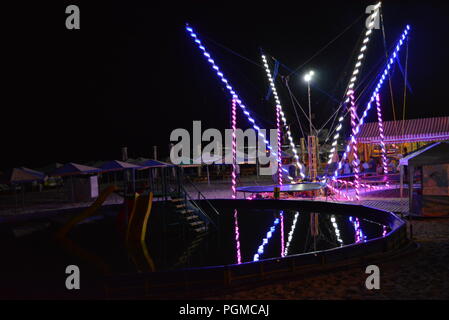 Am Strand des Schwarzen Meeres mit Kinderbecken, Trampolin mit Diodenbändern und Sonnenschirmen entlang der Küste. Stockfoto