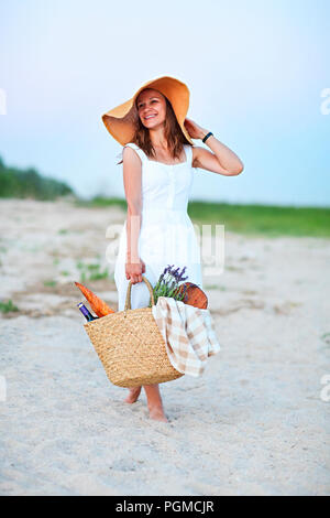 Junge Frau mit Picknickkorb mit einer Flasche Wein und Baguette auf Sand Strand Stockfoto