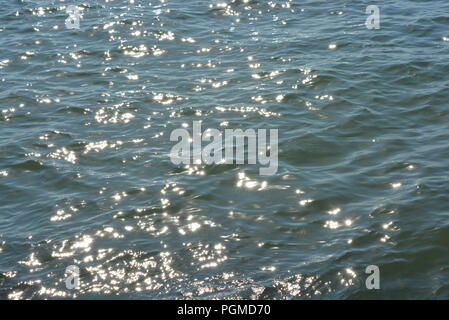 Tiefblaues, schwarzes Meer mit kleinen Wellen und kleinen goldenen und hellen Sonnenspiegeln auf einem Meeresgrund. Stockfoto