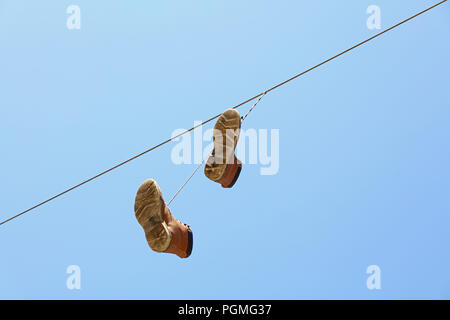 Paar alte abgenutzte braune Stiefel hängend an einer Telefonleitung Draht, wie traditionelle städtische Jugend Witz, über klaren blauen Himmel, Low Angle View Stockfoto