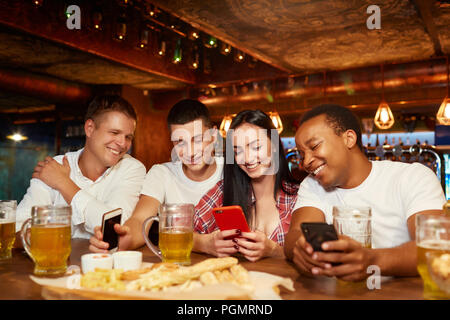 Gerne Freunde mit Smartphone und Spaß mit Bier und Snacks an der stilvollen Pub. Um jungen Mädchen mit Gadgets in Händen sitzen, ihre Videos Stockfoto