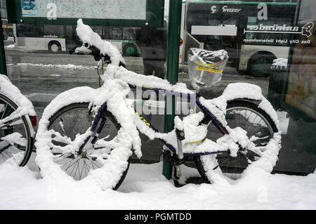 Ein schneebedecktes Fahrrad wurde an einen Posten an einem Bus-/Straßenbahnterminal in der Nähe des Grazer Bahnhofs in Graz, Österreich, angekettet. Stockfoto