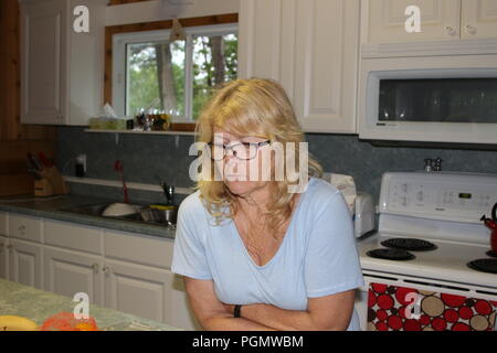 Close up Nachdenklich im mittleren Alter blonde Frau, sitzen im Wohnzimmer und sah mit den Händen auf das Kinn. Stockfoto