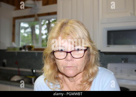 Close up Nachdenklich im mittleren Alter blonde Frau, sitzen im Wohnzimmer und sah mit den Händen auf das Kinn. Stockfoto