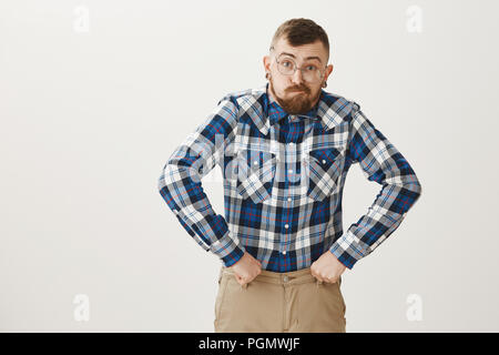 Kerl erhielt Alten zu schnell. Lustige begabten männlichen Schauspieler in Gläsern und Blue Plaid Shirt nachahmen, Großvater, Gesichter machen und mit geballten Fäusten in der Nähe der Hüfte in Urkomischen darstellen, stehen über graue Wand Stockfoto
