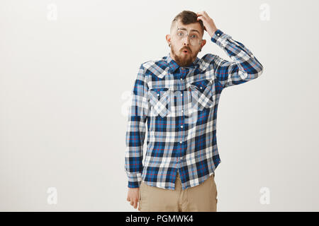 Studio shot von dumm stattlicher Mann in Plaid Shirt und Brille, kratzen Kopf und Falten Lippen beim Sagen wow, verwirrt und im Mathematikunterricht clueless, haben keine Ahnung von Thema Stockfoto