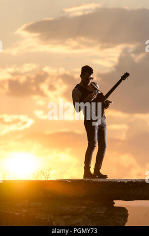 Mann führt auf E-Gitarre auf alten römischen Aquädukt während des Sonnenuntergangs. Stockfoto