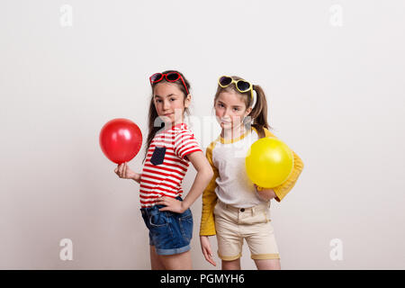 Kleine Mädchen mit Sonnenbrille und Luftballons in einem Studio. Stockfoto