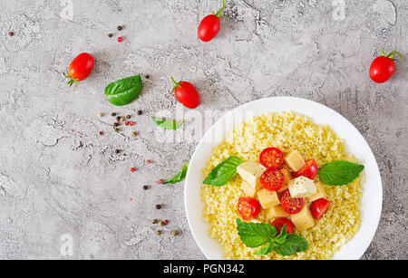 Millet Porridge mit Käse, Butter und Basilikum in weiße Schüssel. Leckeres Essen. Frühstück. Ansicht von oben. Flach Stockfoto