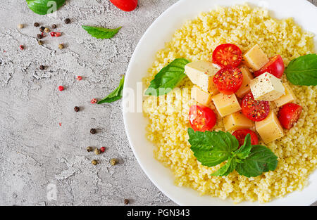 Millet Porridge mit Käse, Butter und Basilikum in weiße Schüssel. Leckeres Essen. Frühstück. Ansicht von oben. Flach Stockfoto