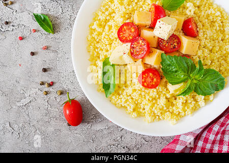 Millet Porridge mit Käse, Butter und Basilikum in weiße Schüssel. Leckeres Essen. Frühstück. Ansicht von oben. Flach Stockfoto