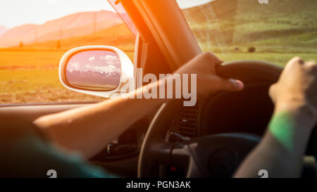Auto auf der Mountain Road. Kerl im Auto Fahren auf der Fahrbahn zwischen Feldern mit braunem Gras und schneebedeckten Berge. Sun ist shini Stockfoto