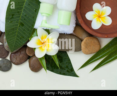 Wellness Hintergrund mit weißer Bettwäsche, tropische Blätter, Blumen, Körper- und Gesichtspflege Tools, Steine und Zubehör auf weißem Hintergrund, Ansicht von oben. Stockfoto