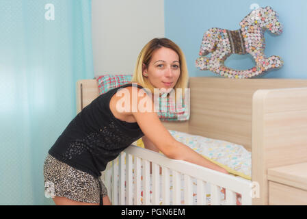 Junge Frau, die ihr Baby Kinderbett Stockfoto