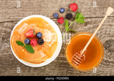 Pfannkuchen mit verschiedenen Beeren und Honig auf alten hölzernen Hintergrund stack. Ansicht von oben. Flach Stockfoto