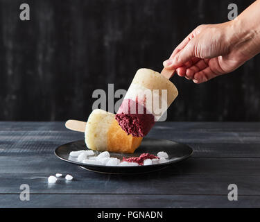 Eine Frau nimmt eine fruchtig Kaffee hausgemachtes Eis lolly in eine schwarze Platte mit Eiswürfel auf einem dunklen Hintergrund mit kopieren. Diätetische Dessert Stockfoto
