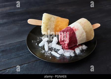 Obst Kaffee hausgemachtes Eis lolly auf einem Stick in eine schwarze Platte mit Scheiben von Eis auf einem dunklen Holz Tisch mit kopieren. Kaltes Dessert Stockfoto