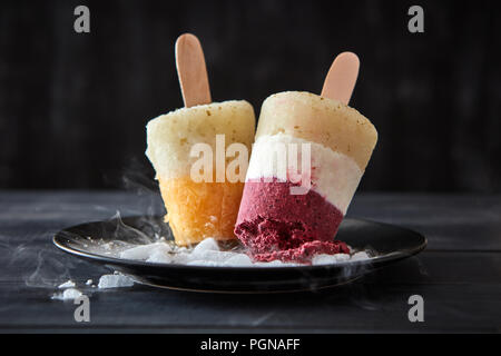 Berry sorbet Lolly auf einem Stick in eine Platte mit Scheiben von Eis auf einem schwarzen Holz- Hintergrund. Diätetische Dessert Stockfoto