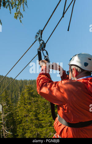 Mann hält an Zip Line Hardware in Orange Anzug und weissen Helm Stockfoto