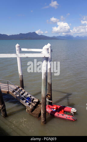 Laden Gang vom Steg in den roten Schlauchboot mit Hinchinbrook Island und Hinchinbrook Channel im Hintergrund, Cardwell, Queensland, Australien. Keine Stockfoto