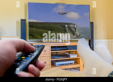 Mann mit Füßen mit Fernbedienung TV-Kanäle zu ändern. Stockfoto