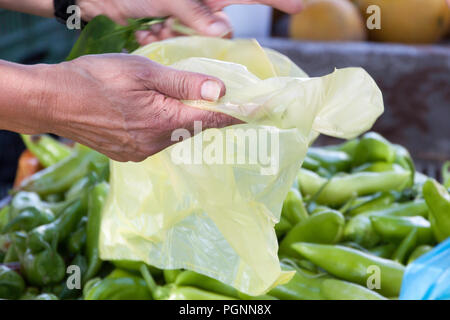 Eine Hand, die eine Leere gelbe Plastiktüte über grüne Paprika in Lebensmittelgeschäft Stockfoto