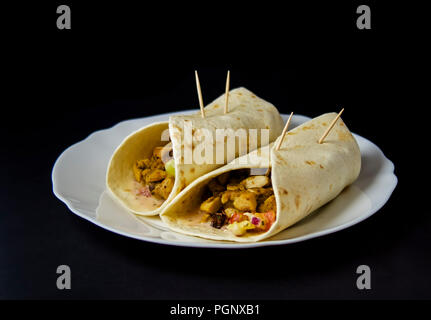 Hausgemachte Burrito mit Hähnchen und Gemüse auf schwarzem Hintergrund isoliert. Burritos sind ein traditionelles Essen in Ciudad Juárez, einer Stadt an der Grenze zu El Paso, T Stockfoto