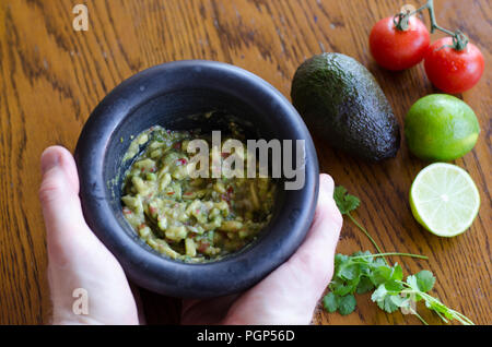 Die Guacamole in einem Mörser mit den Zutaten, die auf dem Hintergrund Stockfoto