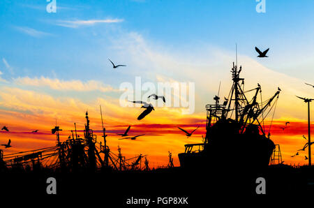 Angeln Boote und Vögel in Schwarz gegen eine lebendige Sonnenuntergang in Orange, Rot, gelben und blauen Himmel. Schöne nautischen Szene. Marokko. Stockfoto