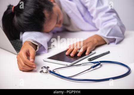 Junge Ärztin Schlafen an ihrem Schreibtisch arbeiten über Laptop und Bericht Papier dokumentieren, wer in der Klinik müde fühlen überfordert., nachdem er den ganzen Tag arbeiten Alle Stockfoto