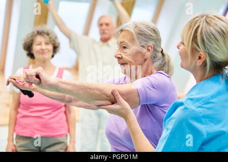 Ältere Frau in Physiotherapie ist dabei Übung mit Gummizug mit Hilfe der Trainer Stockfoto