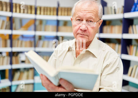 Älterer Mann liest in einem Buch und bildet sich in der Bibliothek im Pflegeheim Stockfoto