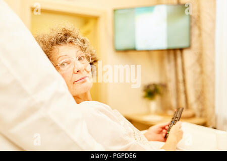 Alte Frau im Altersheim oder Senioren Apartment liegt im Bett fernsehen Stockfoto