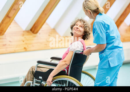 Ältere Frau als ein Patient in einem Rollstuhl wird gepflegt, durch einen Betreuer an der REHA-Klinik Stockfoto