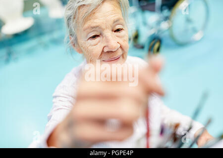 Alte Frau mit Demenz in einem malkurs in der Therapie im Pflegeheim Stockfoto