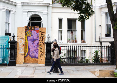 London, Großbritannien. 27 Aug, 2018. Ein paar gesehen vorbei gehen die Zugenagelten Tor zu einem Haus als Nachtschwärmer und paraders durch die Straßen von Notting Hill in West London pack. Hunderttausende für den wichtigsten Tag der Notting Hill Carnival, der jährlich seit 1964 stattgefunden hat. Quelle: David Cliff/SOPA Images/ZUMA Draht/Alamy leben Nachrichten Stockfoto