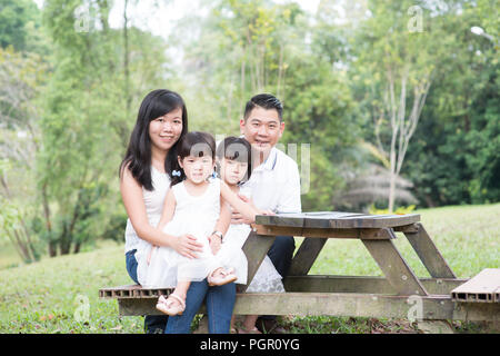 Asiatische Familie Portrait. Eltern und Kinder im Park sitzen. Leeren Raum auf Holztisch. Stockfoto