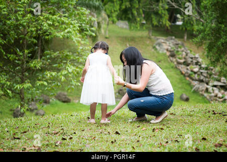 Mutter hilft, kleine Mädchen Schuh tragen im Green Park. Asiatische Familie im Freien portrait. Stockfoto