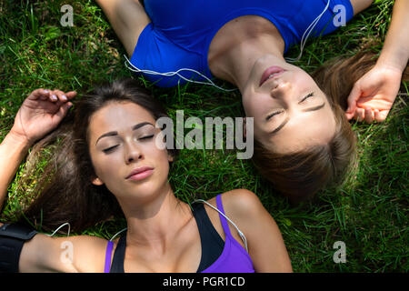 Blick von oben auf die zwei schöne und junge Mädchen mit engen Augen ruhen auf dem Gras nach Outdoor Training an einem sonnigen Tag Stockfoto