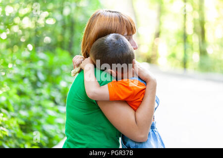 Schöne Frau und ihr kleiner Sohn zittern und stark annehmen, auf City Park Hintergrund. Sommer Portrait von Mutter und Sohn am Muttertag. Stockfoto