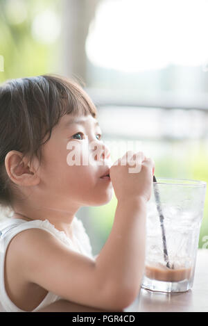 Kleine asiatische Kind trinken Eis Schokolade im Cafe. Natürliches Licht Outdoor Lifestyle. Stockfoto