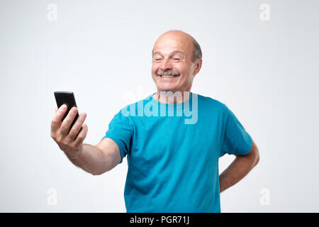 Lächelnd glücklich älterer Mann mit Schnurrbart ein selfie mit seinem Telefon und schicken Sie es an seine Familie. Stockfoto
