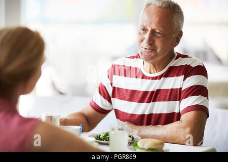 Glücklich im Alter grauhaariger Mann im Gespräch mit seiner Frau vom Mittagessen, während beide sitzen durch serviert Tabelle Stockfoto