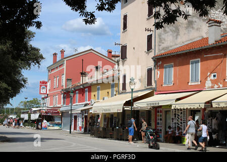 Blick auf die Straße von Fußgängern, die Läden von bunten Gebäude in Rovinj, Rovigno, Kroatien, von Bäumen eingerahmt. Stockfoto