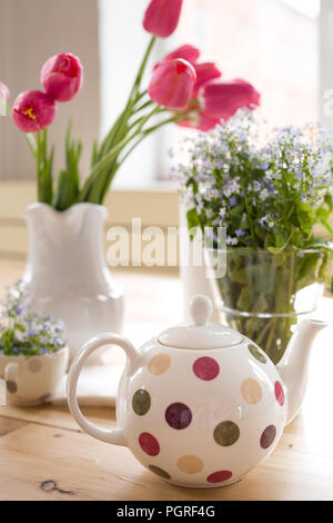 Teekanne mit Dots und Vasen mit schöner Frühling Blumen auf dem Holztisch. Dekoration für zu Hause. Forget-me-not und Tulpen in den Vasen. Blumen Stockfoto