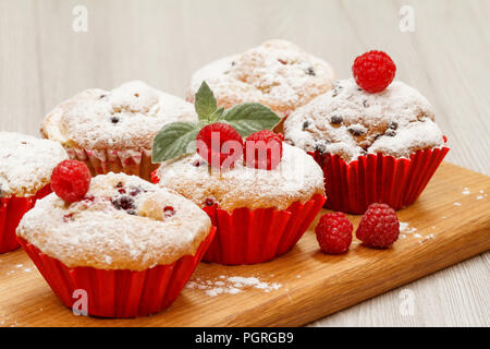 Hausgemachte Frucht Muffins bestreut mit Puderzucker und frische Himbeeren auf Holz Schneidebrett Stockfoto